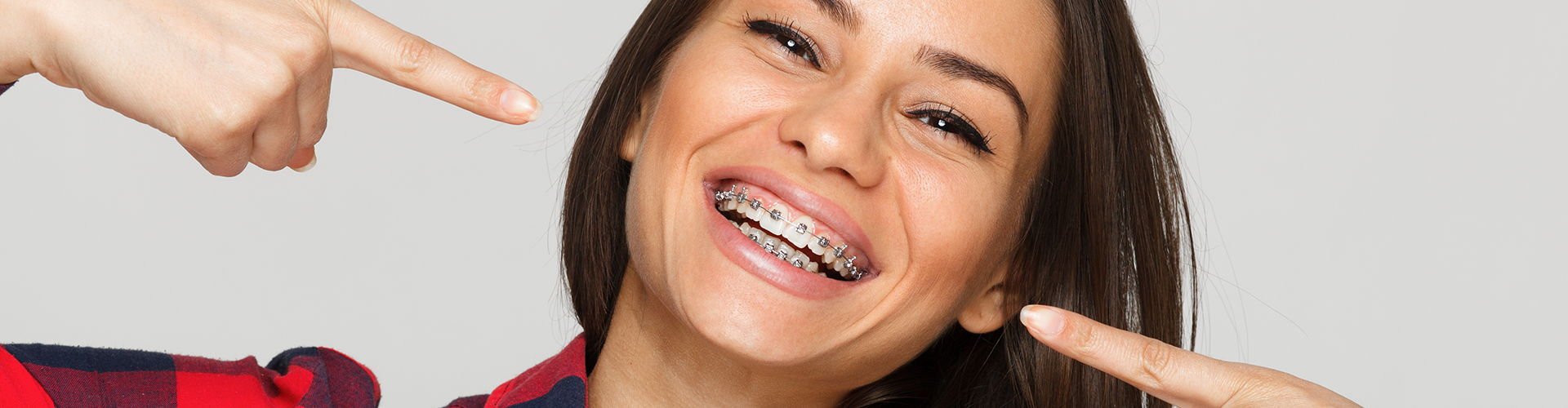 Smiling woman with braces pointing at teeth.